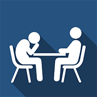 Two people sitting at a table talking to each other.